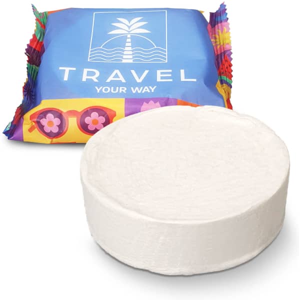 A round white compressed towel in front of colourful packaging featuring a logo.