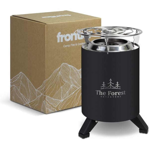 A black camp fire and cooker with a metal top, alongside a cardboard box featuring mountain designs.