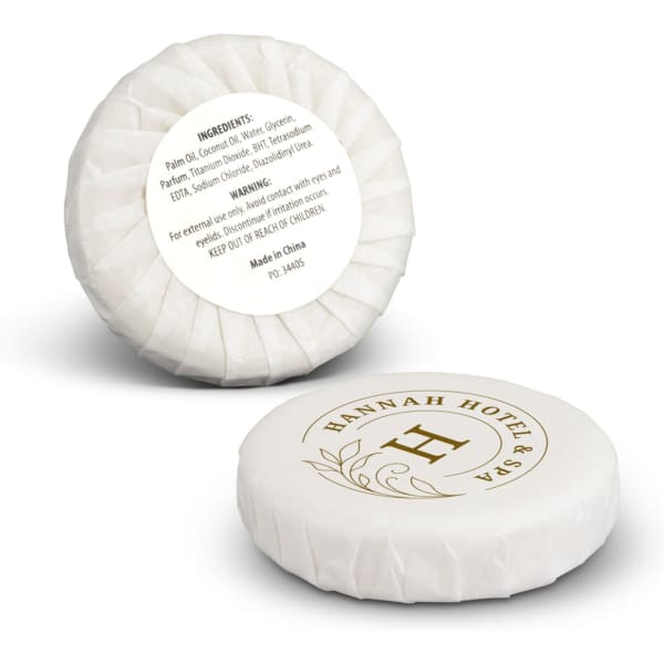 A round white soap bar, wrapped elegantly, featuring a logo and gold detailing, with listed ingredients on the reverse side.
