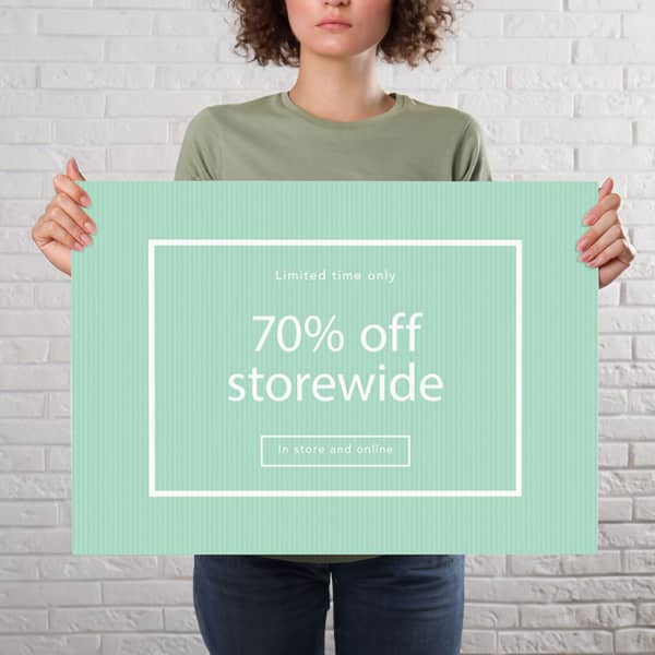 A person holds a large green sign with a white border, featuring a promotional message about storewide discounts.