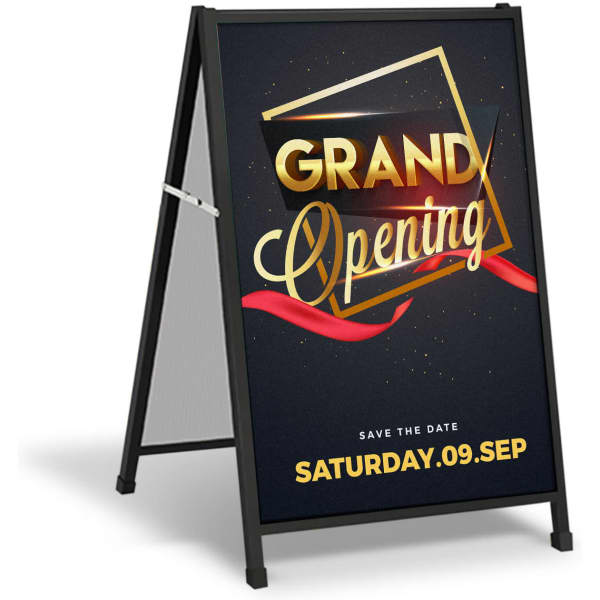 A black A-frame sign featuring a promotional graphic with gold text and a ribbon design for a grand opening event.