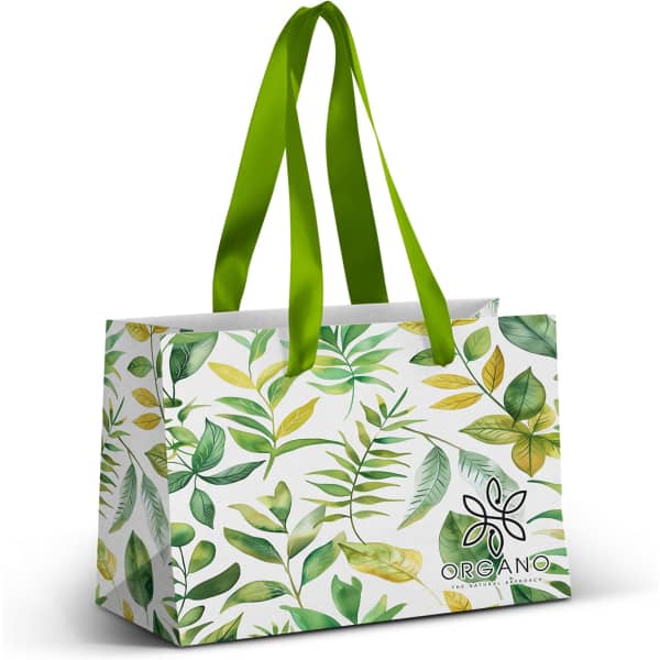 A small paper bag featuring a full-colour design of green leaves, with a green ribbon handle and a logo.