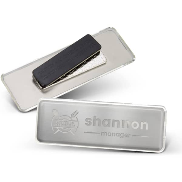 A metal name badge in silver and black, featuring a logo and a smooth surface for engraving.