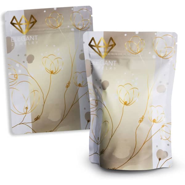A small, elegant foil stand-up pouch in white and gold featuring floral designs and a logo.