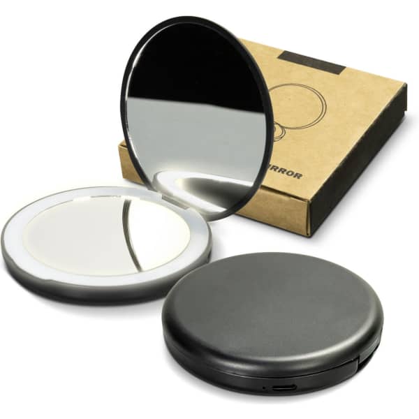 A compact mirror in black, featuring two reflective surfaces, with a cardboard packaging in the background.