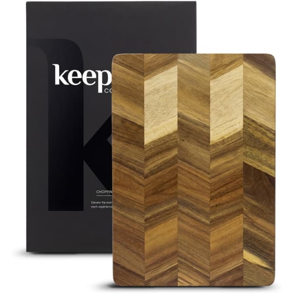 A wooden chopping board with a chevron pattern, presented in a black box with a logo.