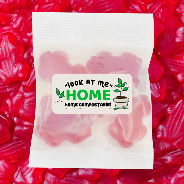 A pack of red gummi frogs, featuring a logo and a label indicating home compostability, against a backdrop of more gummi frogs.