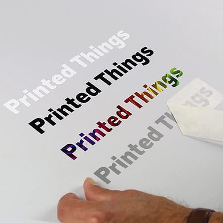 A surface featuring various printed text in multiple colours, with a person's hand preparing a transfer sticker.