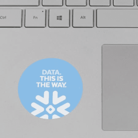 A round laptop sticker in light blue with a snowflake design and white text.