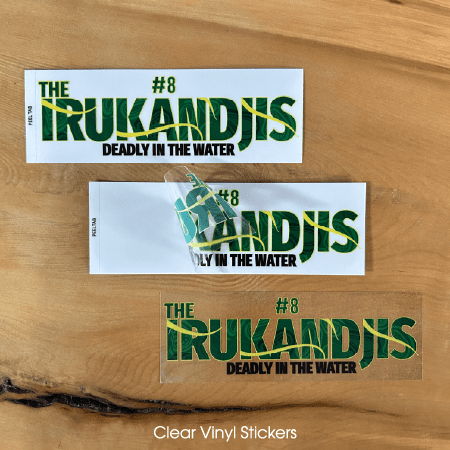 Three clear vinyl stickers featuring the text "The Irukandjis Deadly in the Water" in green and yellow on a wooden surface.