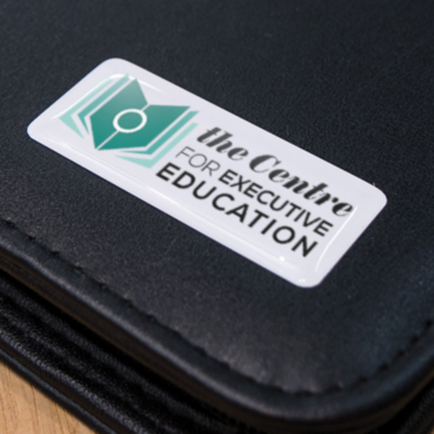 A black folder with a rectangular resin-coated label featuring a logo and text for an education centre.
