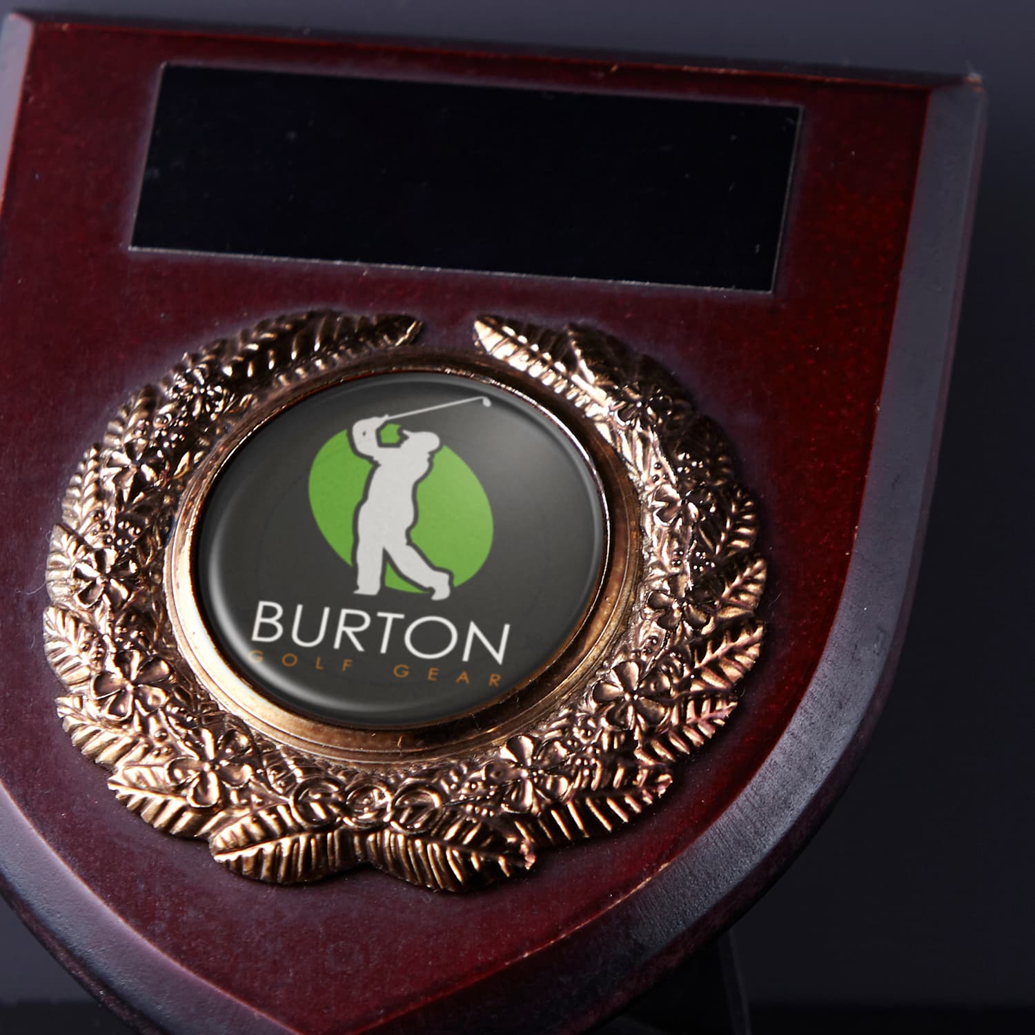 A wooden plaque with a gold laurel wreath and a circular logo featuring a golfer, displaying the brand name.