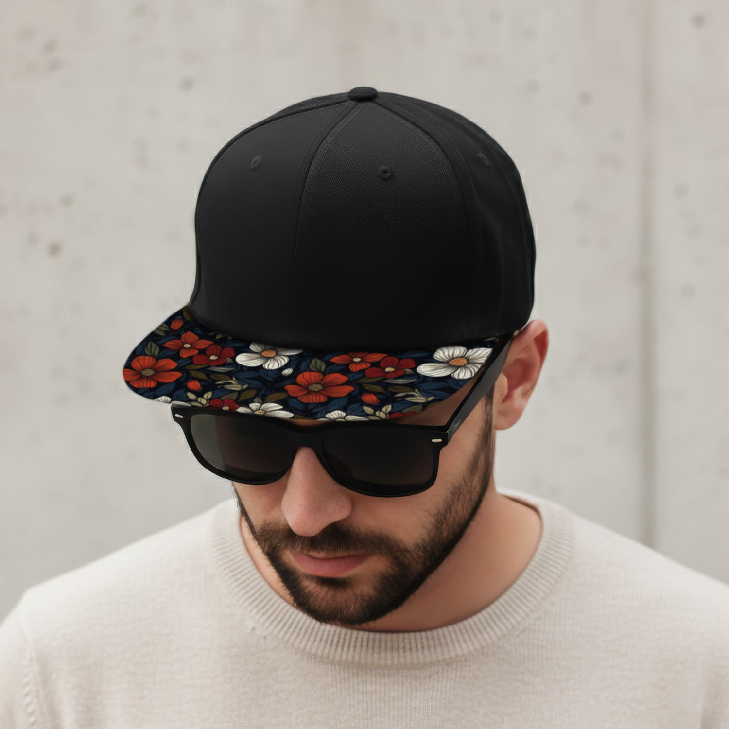 A black flat peak cap with a patterned floral brim, worn by a man in sunglasses.