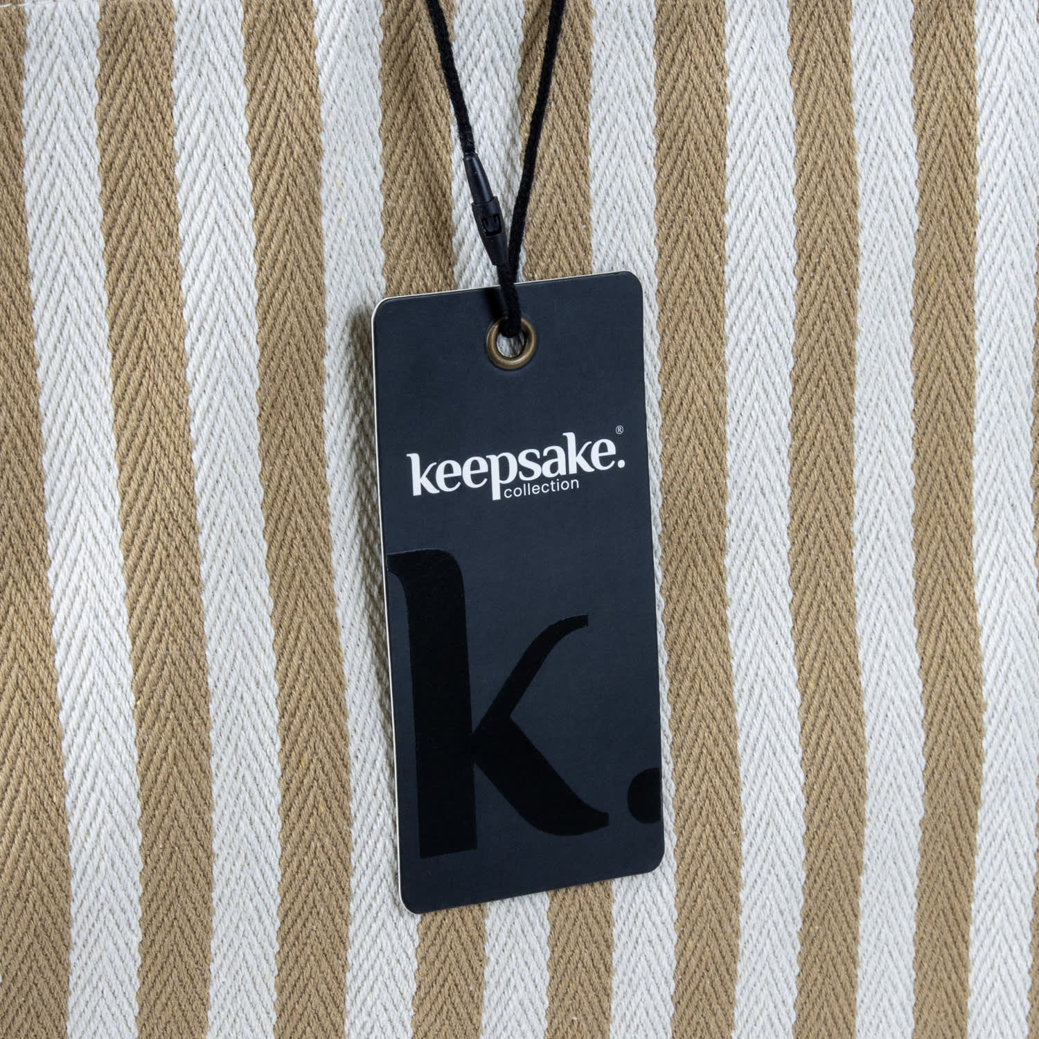 A striped beach tote bag in cream and tan, featuring a tag with a logo attached.