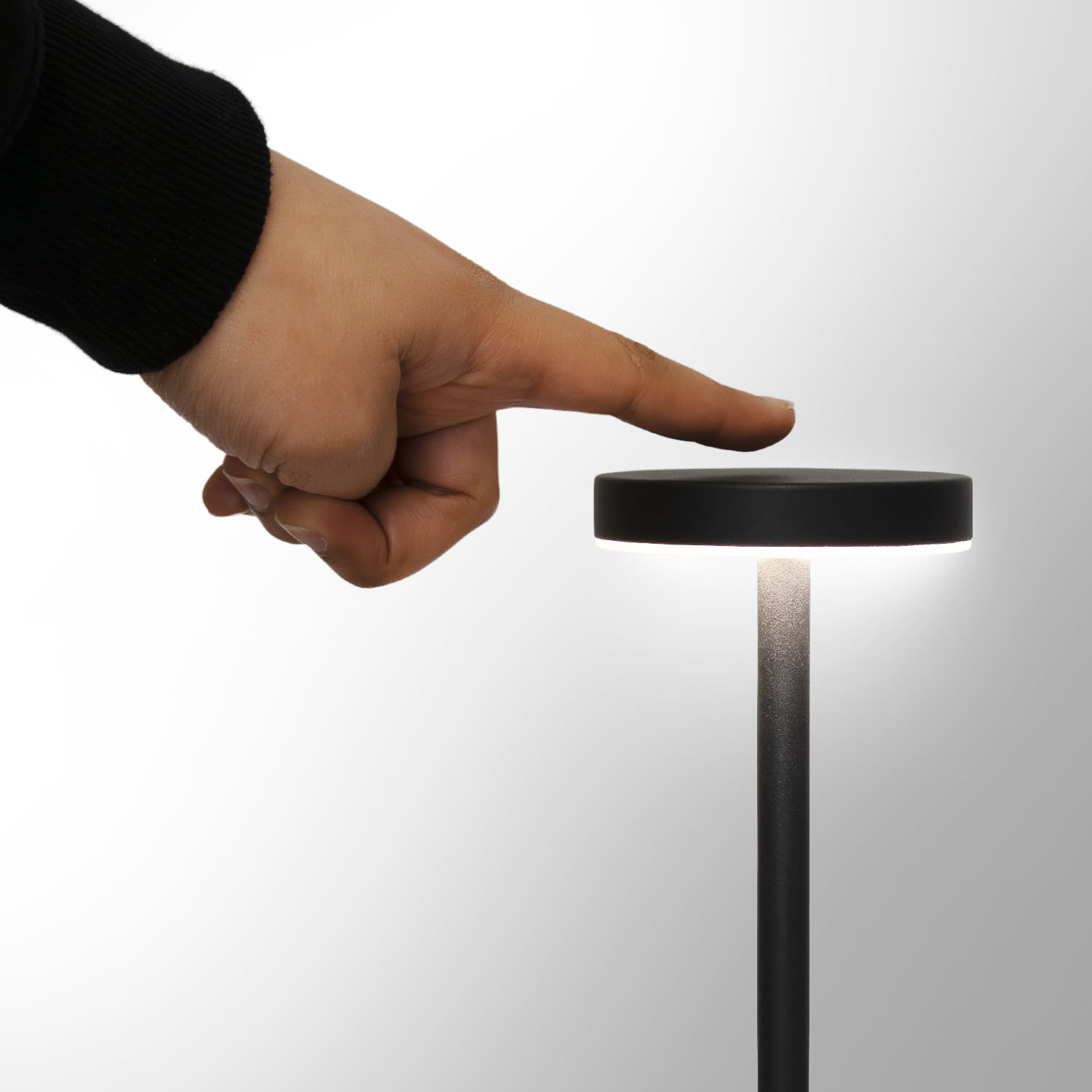 A hand touching the top of a sleek, black rechargeable table lamp with a minimalistic design.