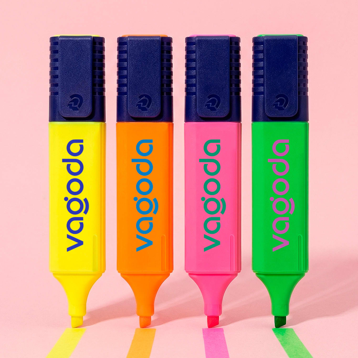 Four highlighters in yellow, orange, pink, and green with a logo on each, resting on a pink surface.