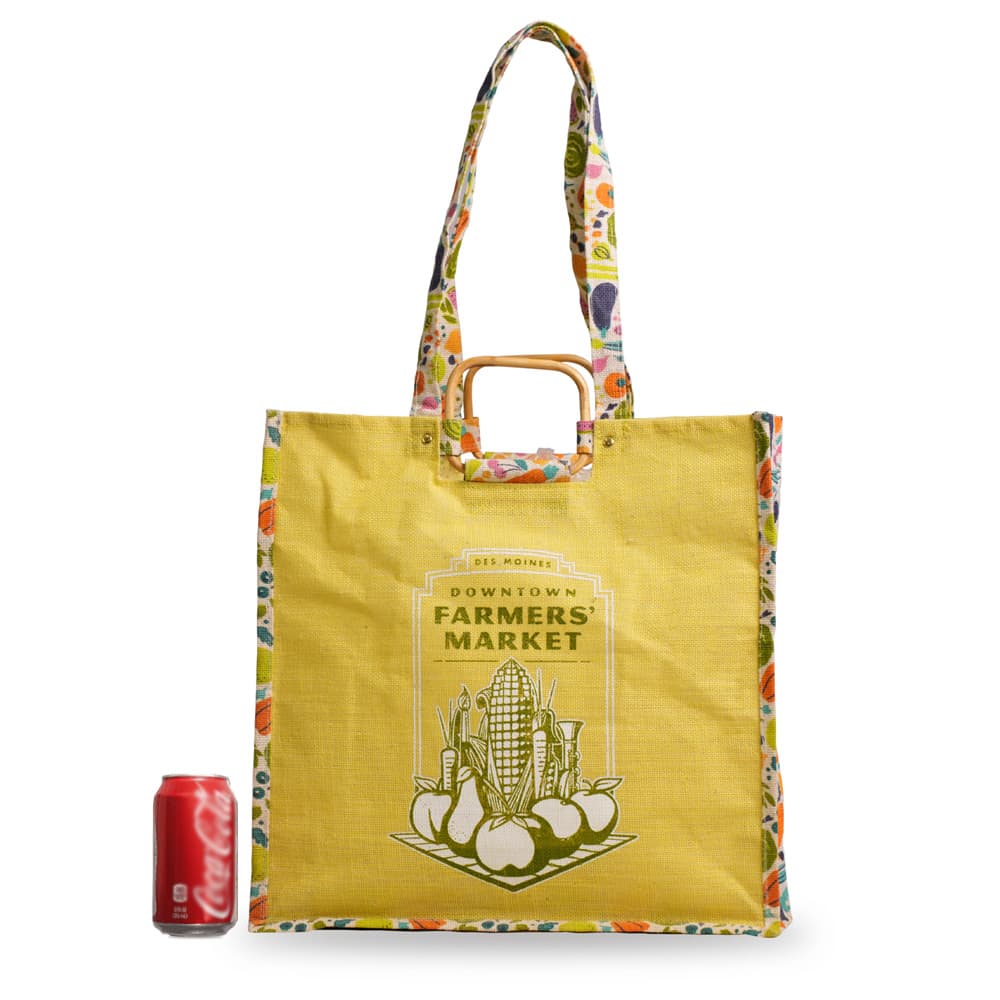 A yellow jute shopping bag with floral accents and a logo, positioned next to a red drink can for scale.