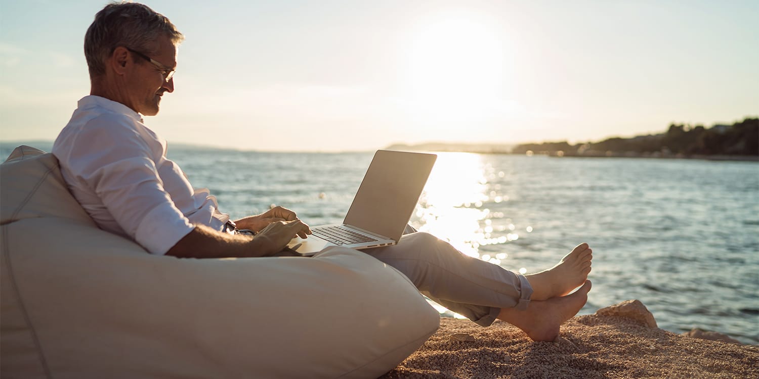Real estate investor sitting on beach looking at investment portfolio