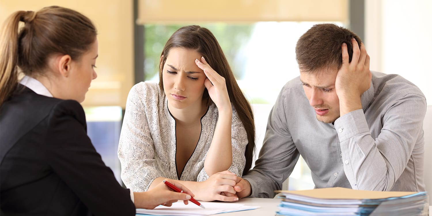 Couple looking dismayed meeting with a real estate agent - home selling mistakes concept.