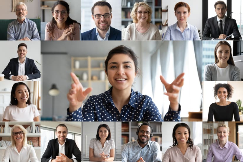 A woman is speaking to a diverse group of people in a virtual meeting, she gestures with her hands at the camera and smiles.