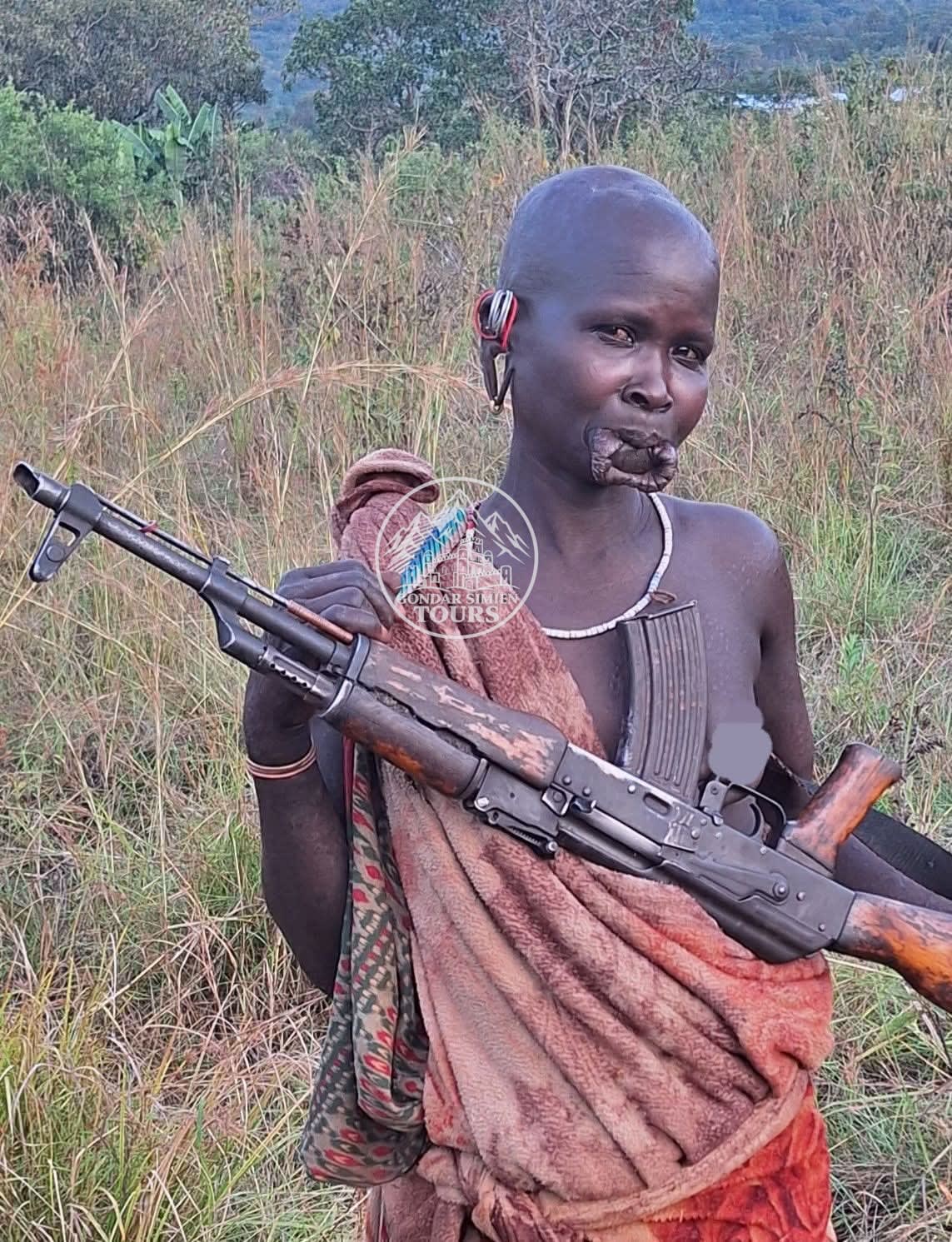 A person in a patterned wrap holding a rifle outdoors