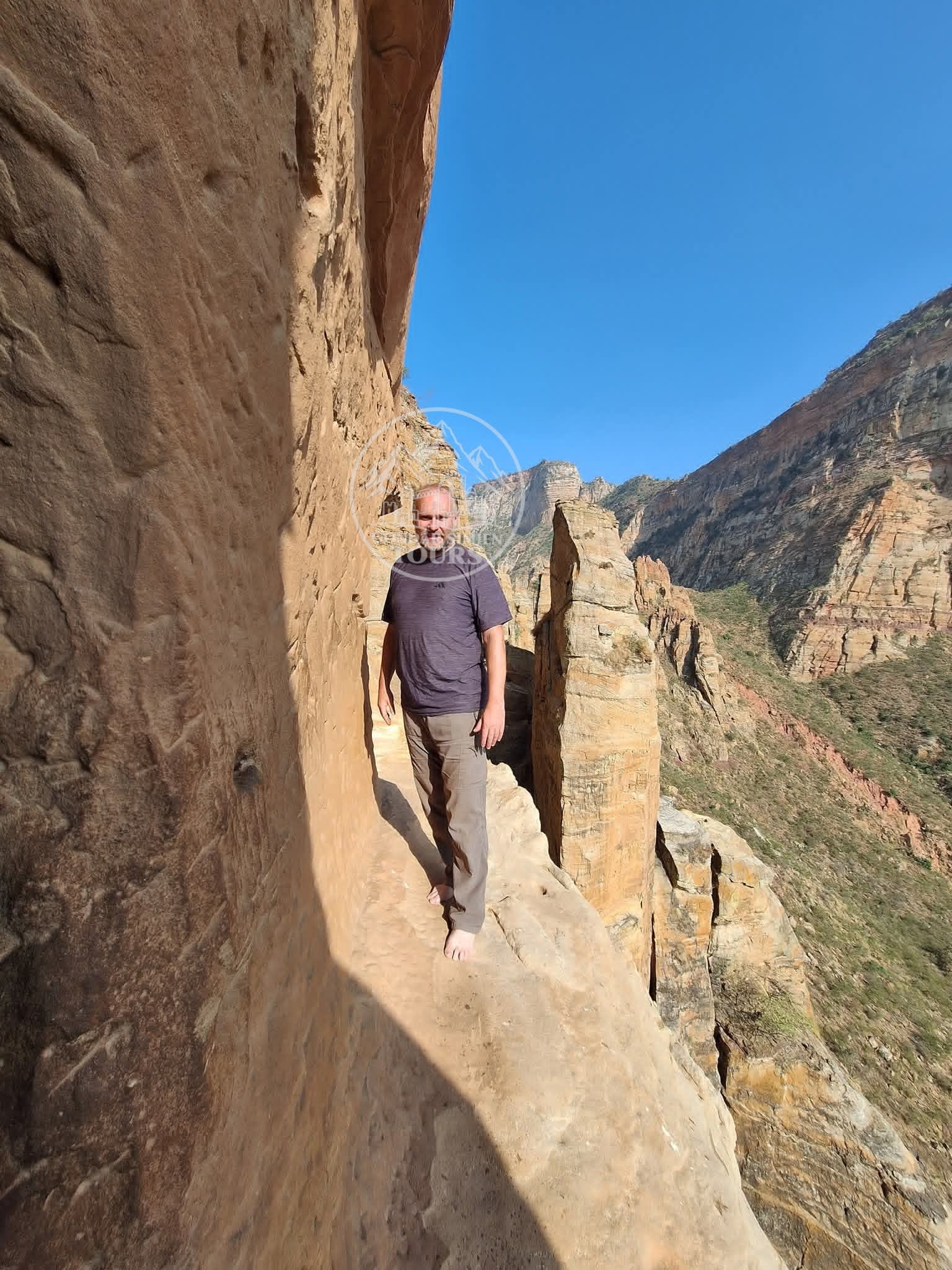 A hiker standing on a narrow path beside a sandstone cliff