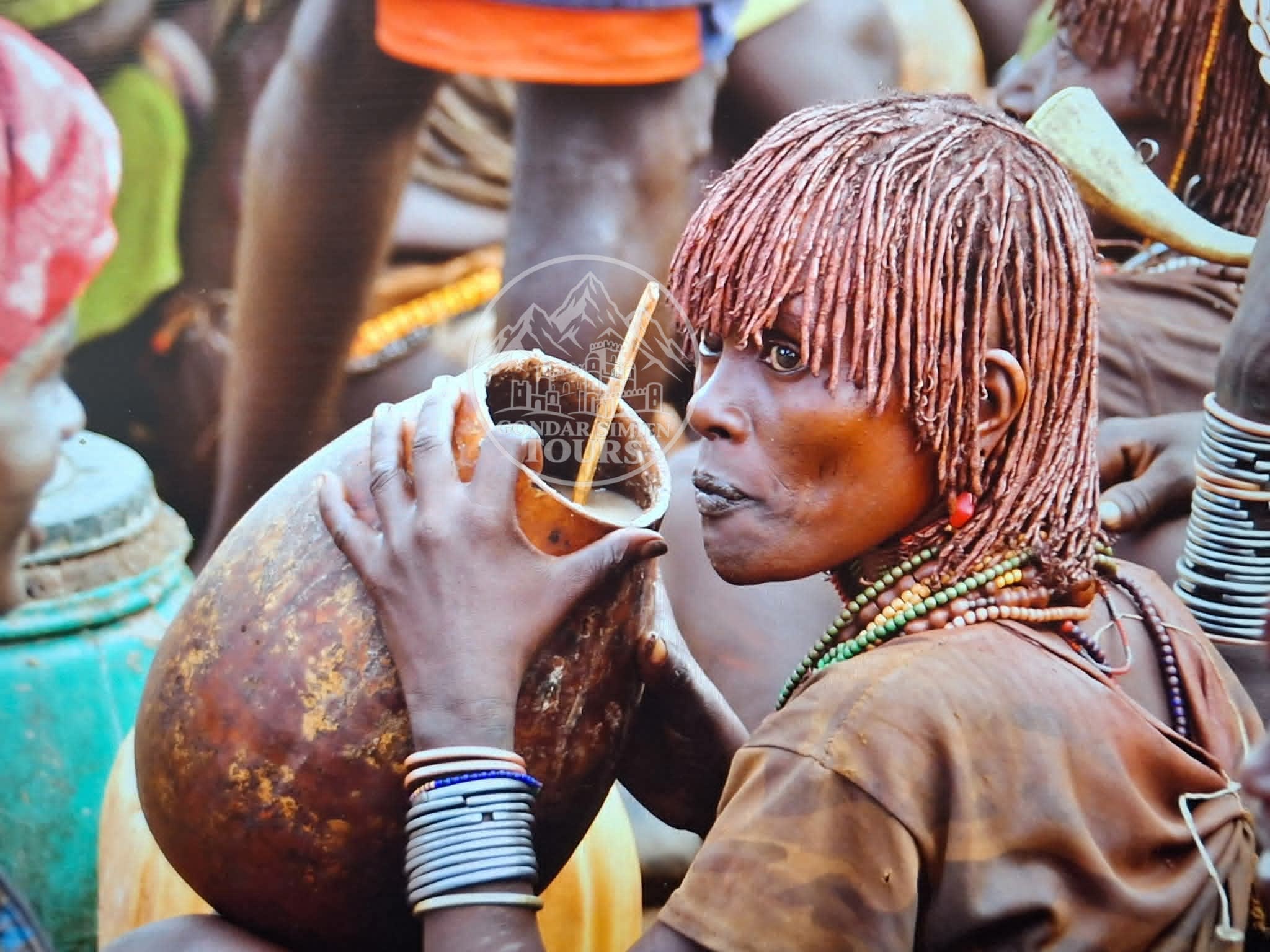 A person with braided hair and bracelets holding a decorated gourd