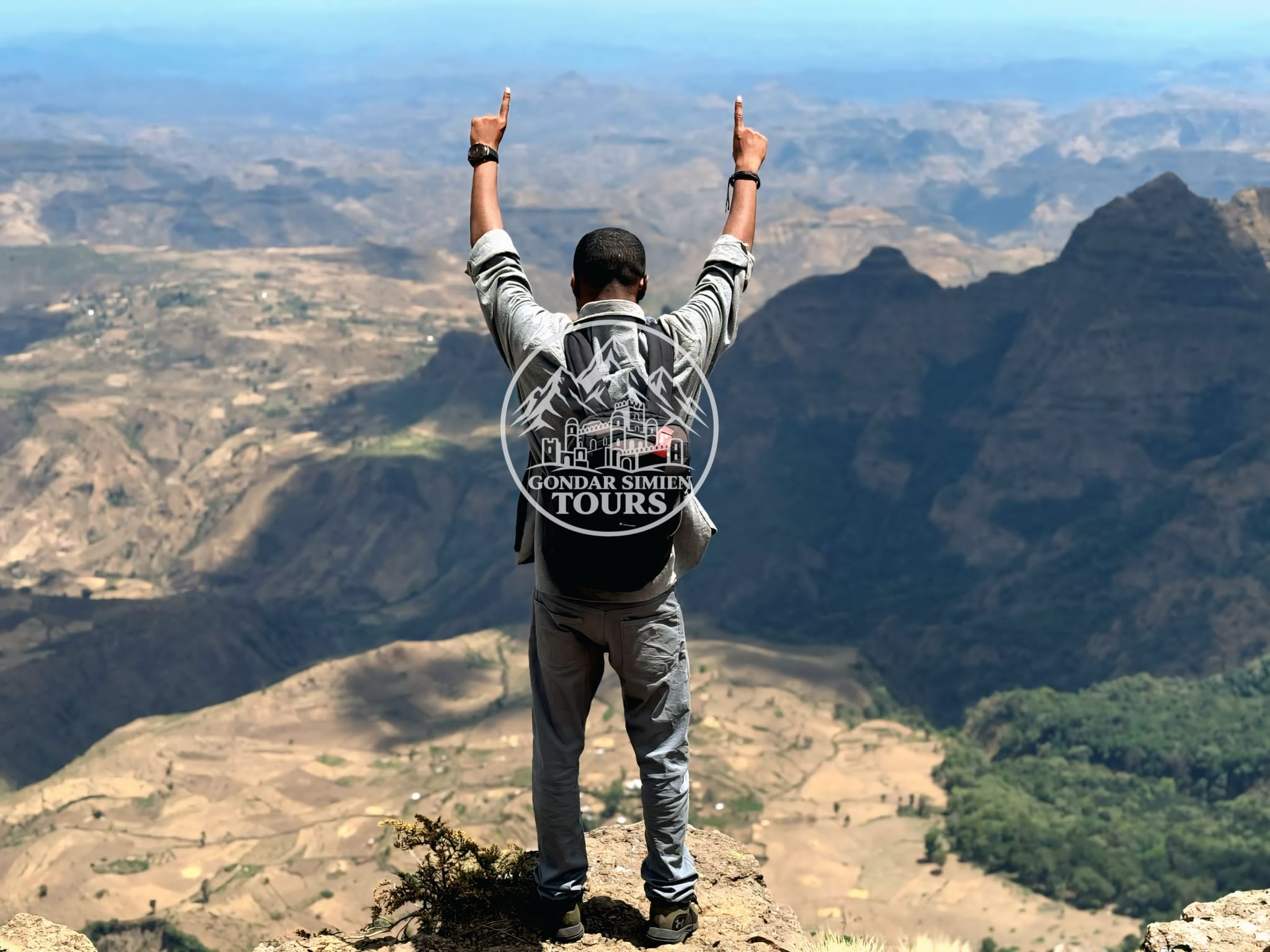A traveller with raised arms overlooking layered mountain valleys