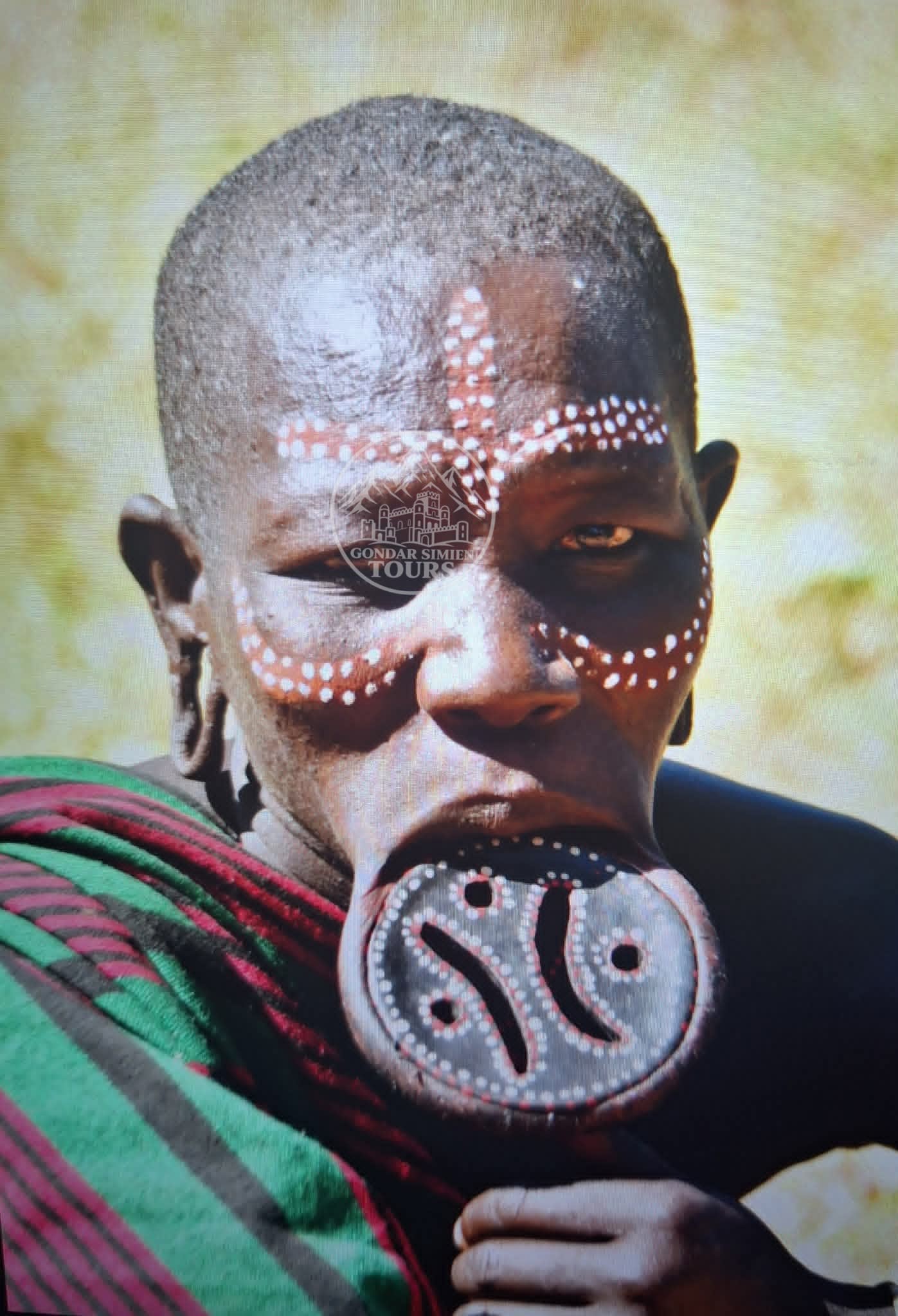 Portrait of a person with painted facial patterns and a decorated lip plate