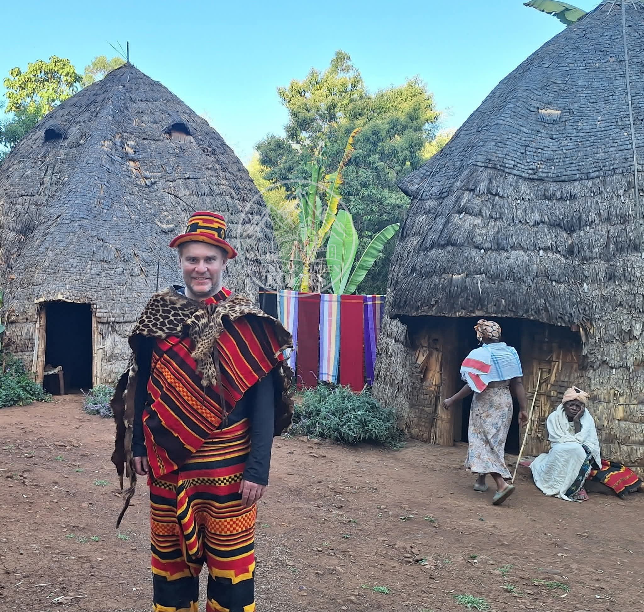 Visitors beside tall woven houses with thatched roofs