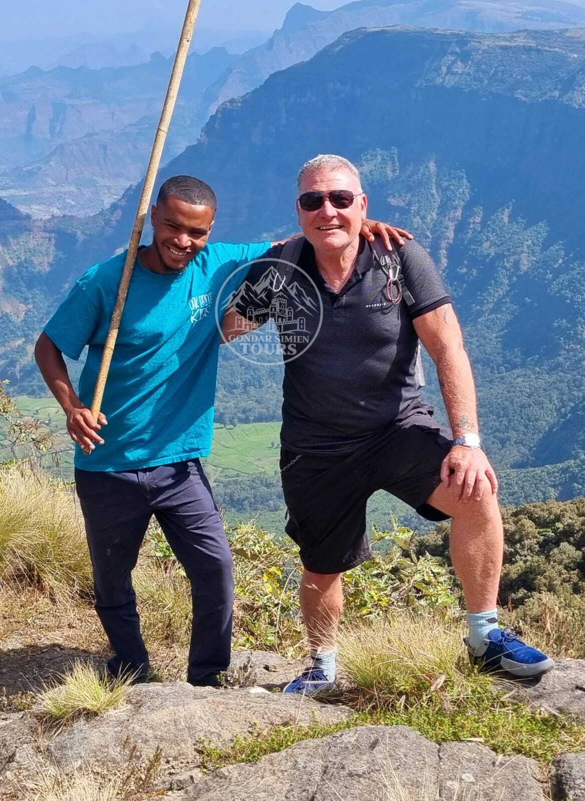Two hikers with walking sticks resting at a mountain viewpoint
