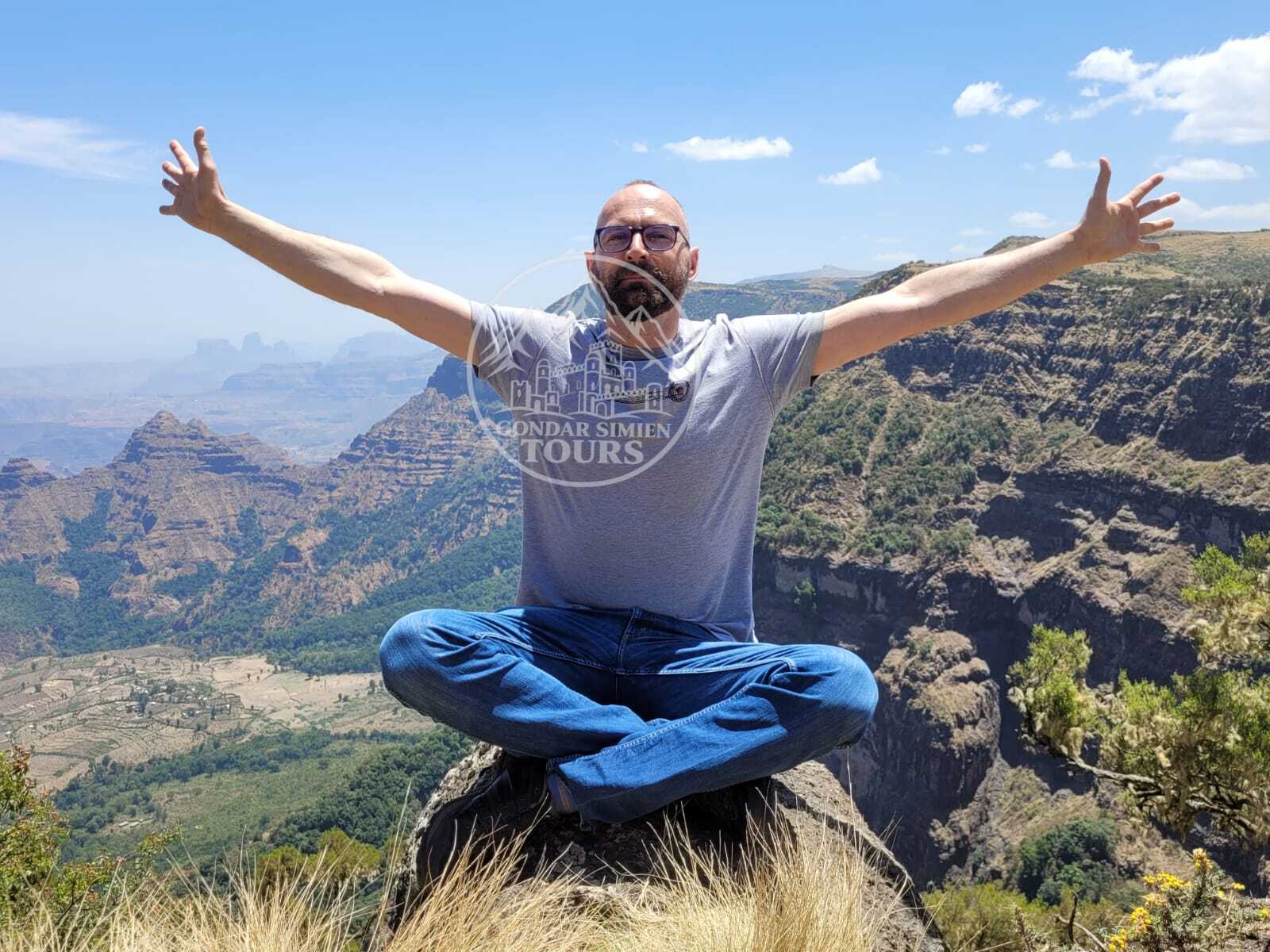 A traveller sitting cross-legged with open arms above a mountain valley