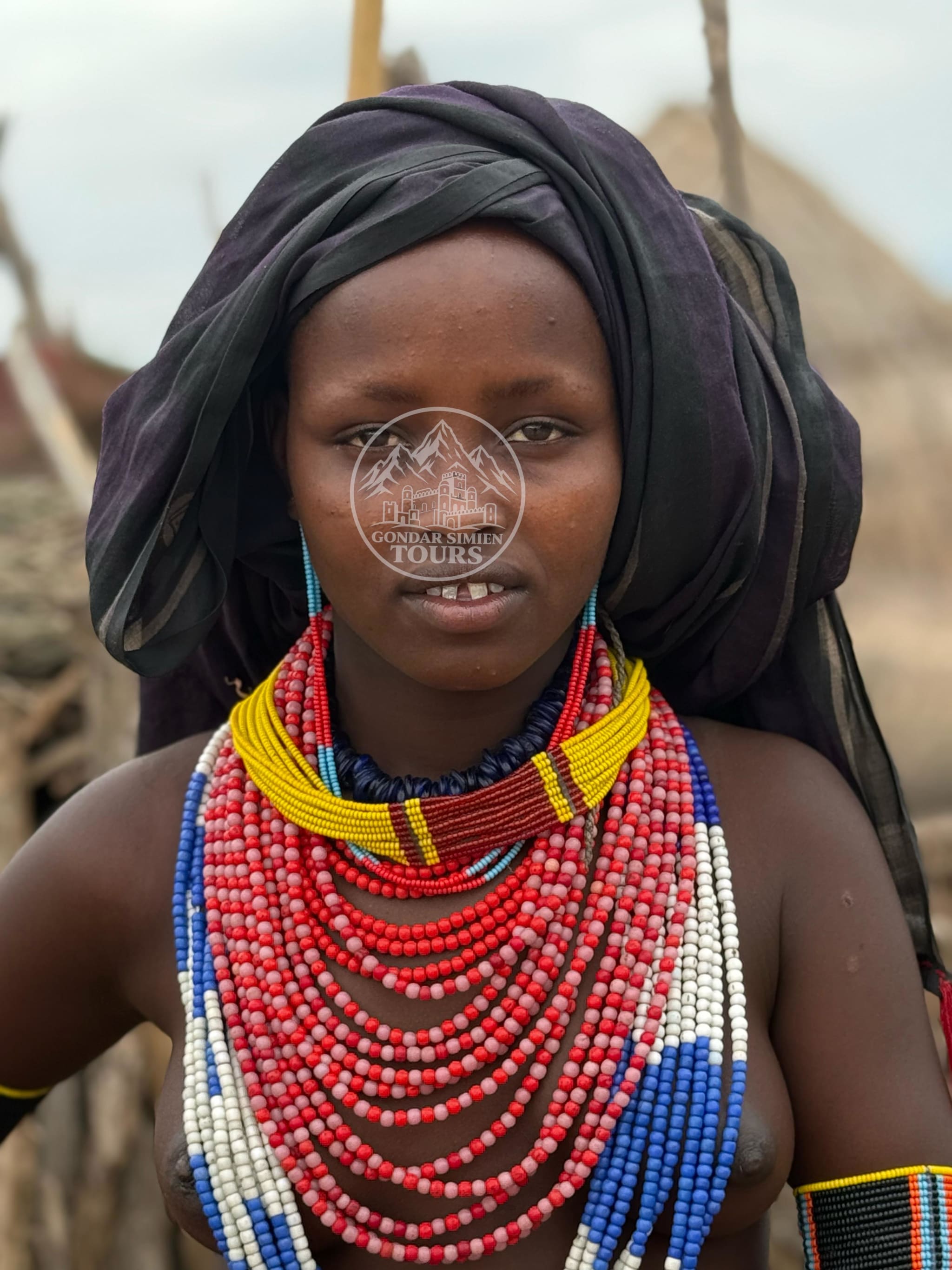 Portrait of a person wearing a dark head covering and layered colourful beads