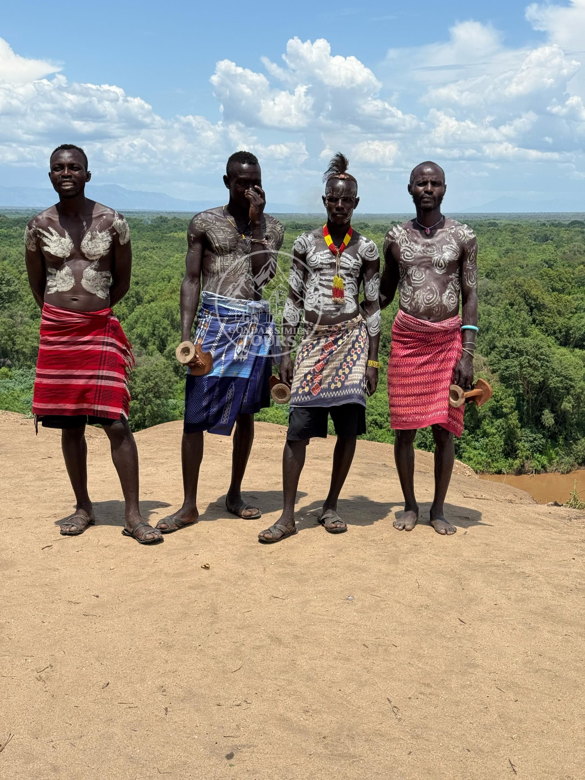 Four people standing together in an open landscape beneath a blue sky