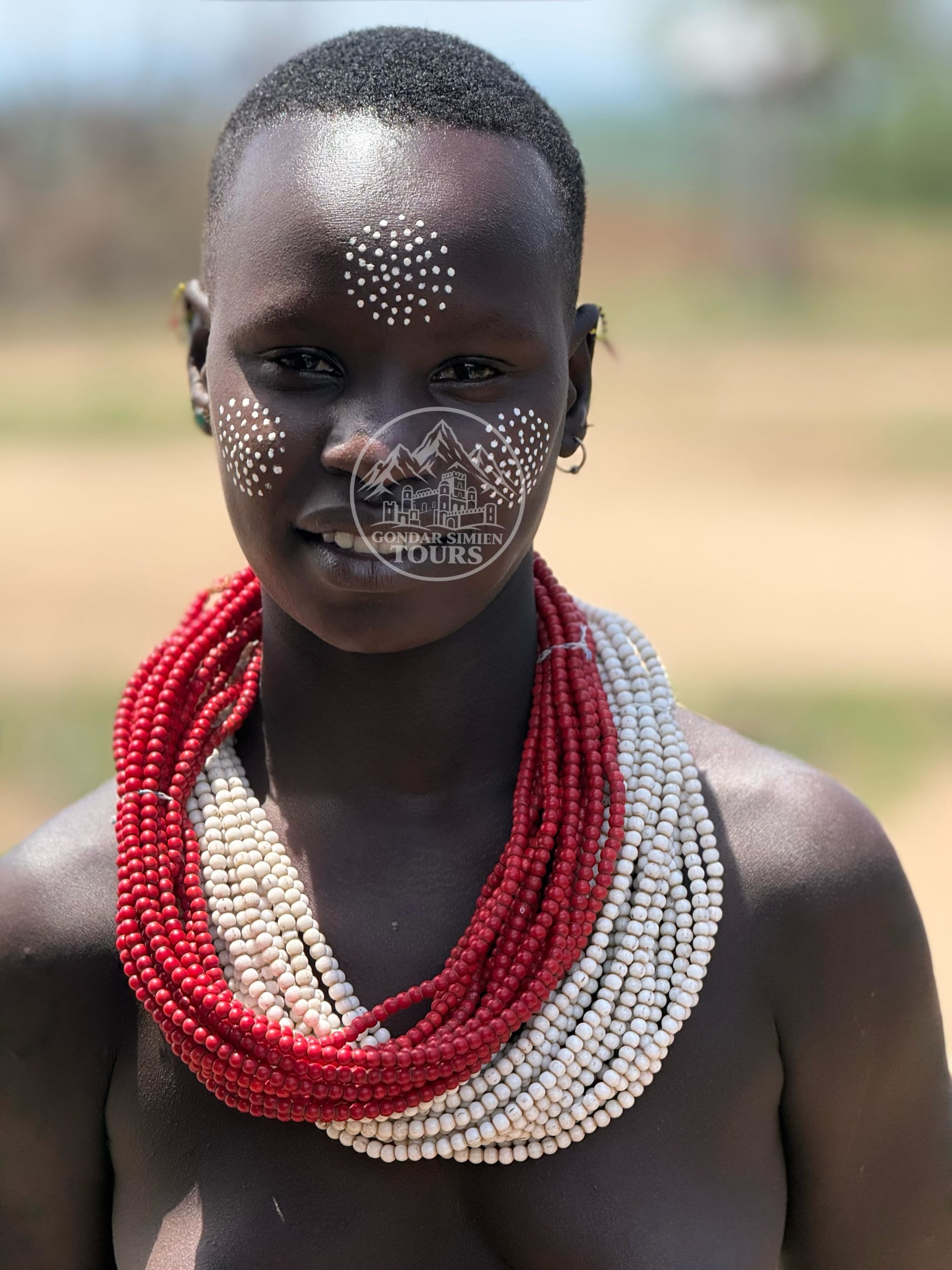 Portrait of a person with painted facial patterns and red and white bead necklaces