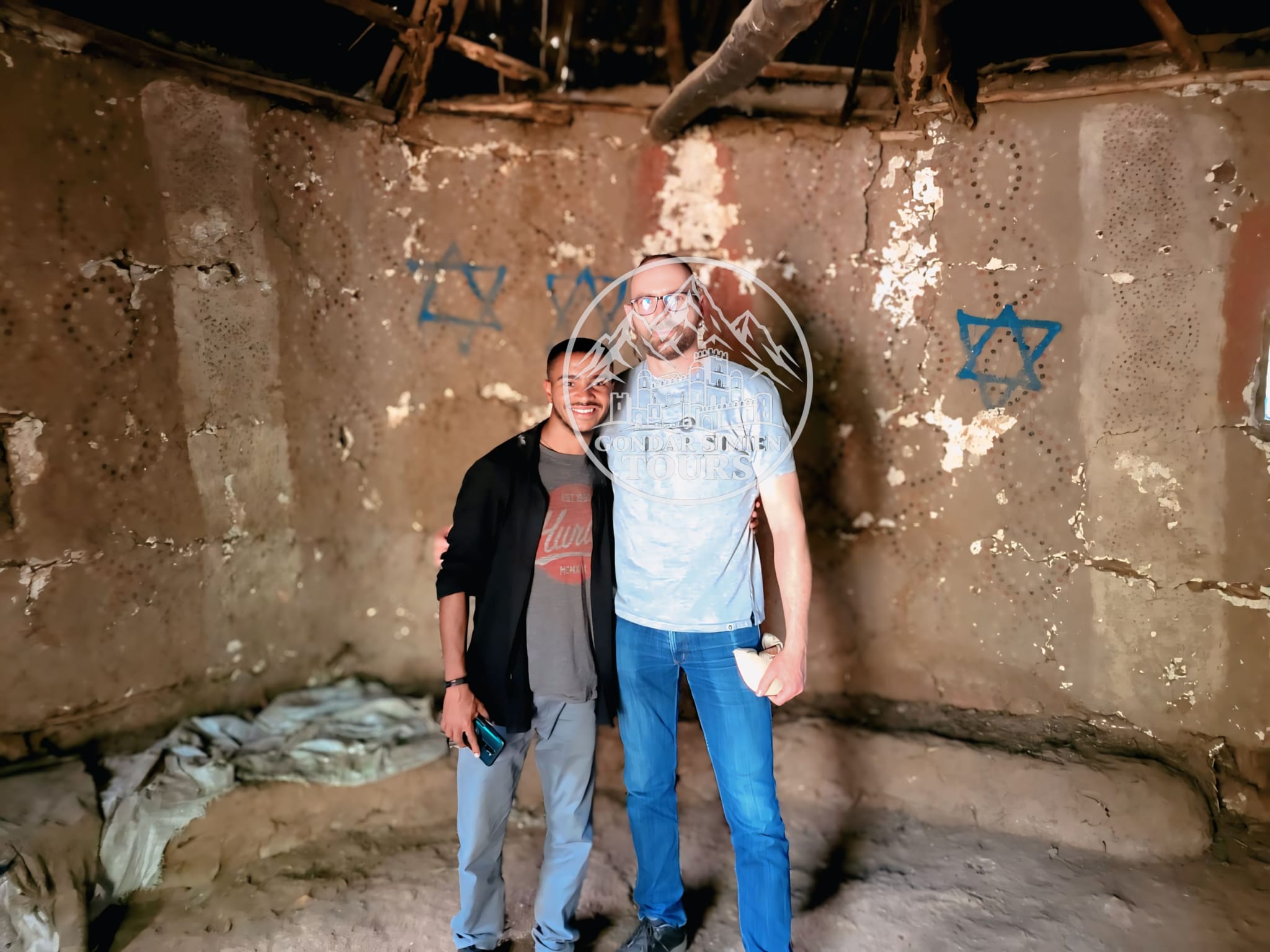 Two visitors standing inside an earthen room with painted wall symbols