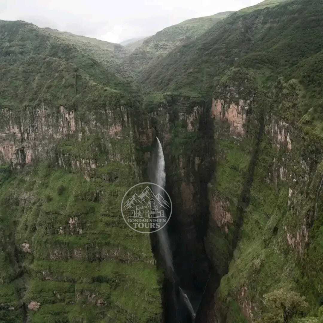 A waterfall descending between green cliffs in the Simien Mountains