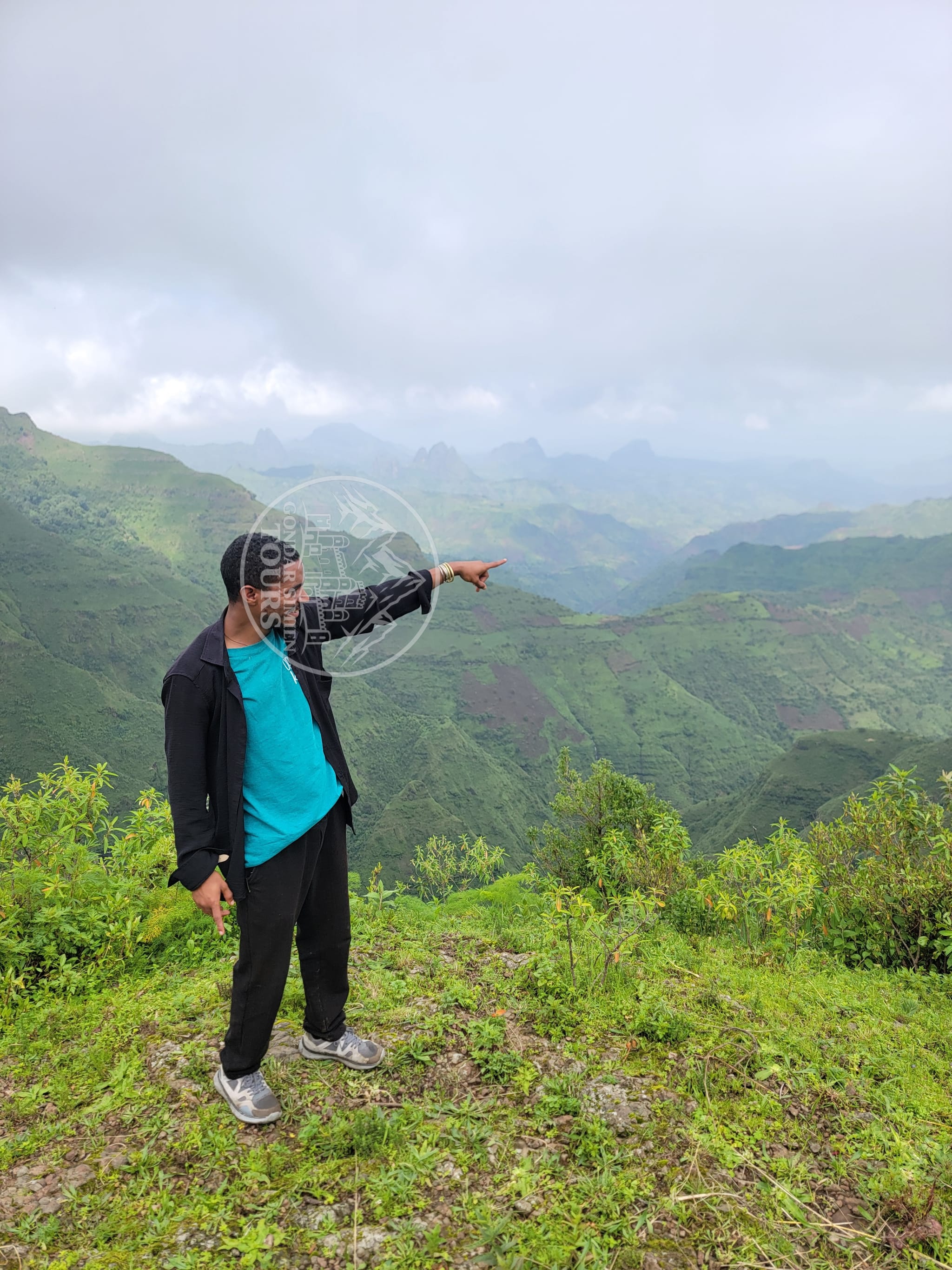 A visitor pointing across the green Kosoye Mountains