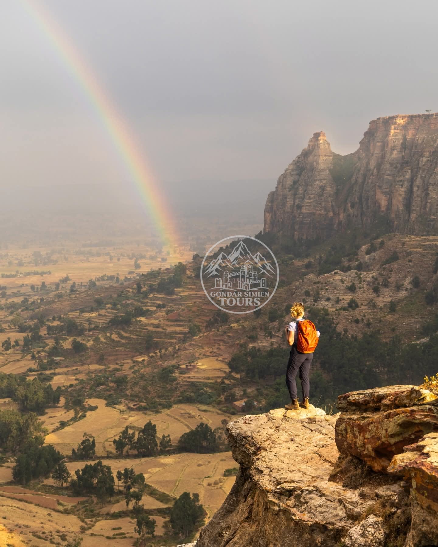 A hiker overlooking terraced highland valleys from a rocky ridge