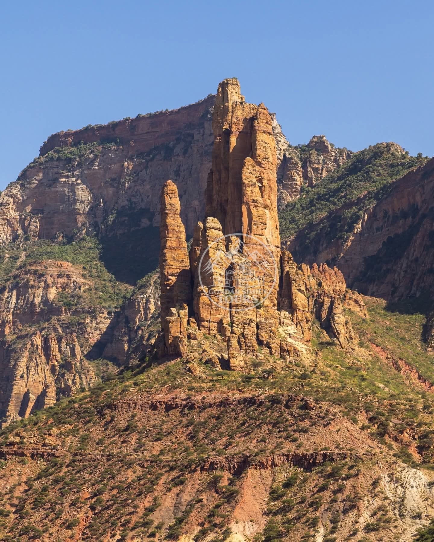 A tall sandstone pillar against mountain ridges under blue sky