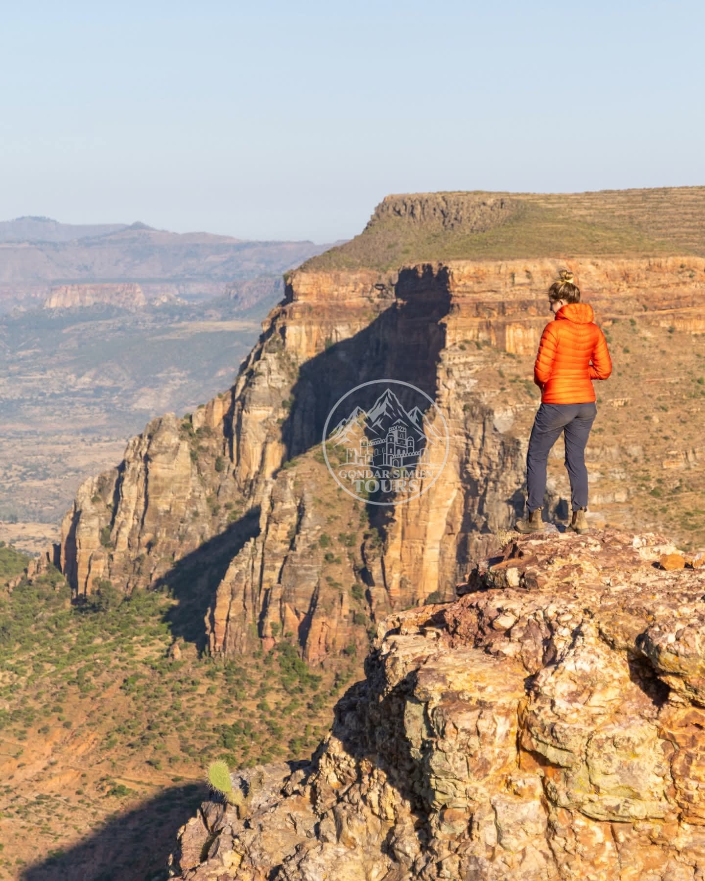 A hiker standing on a rocky cliff edge above layered canyon walls