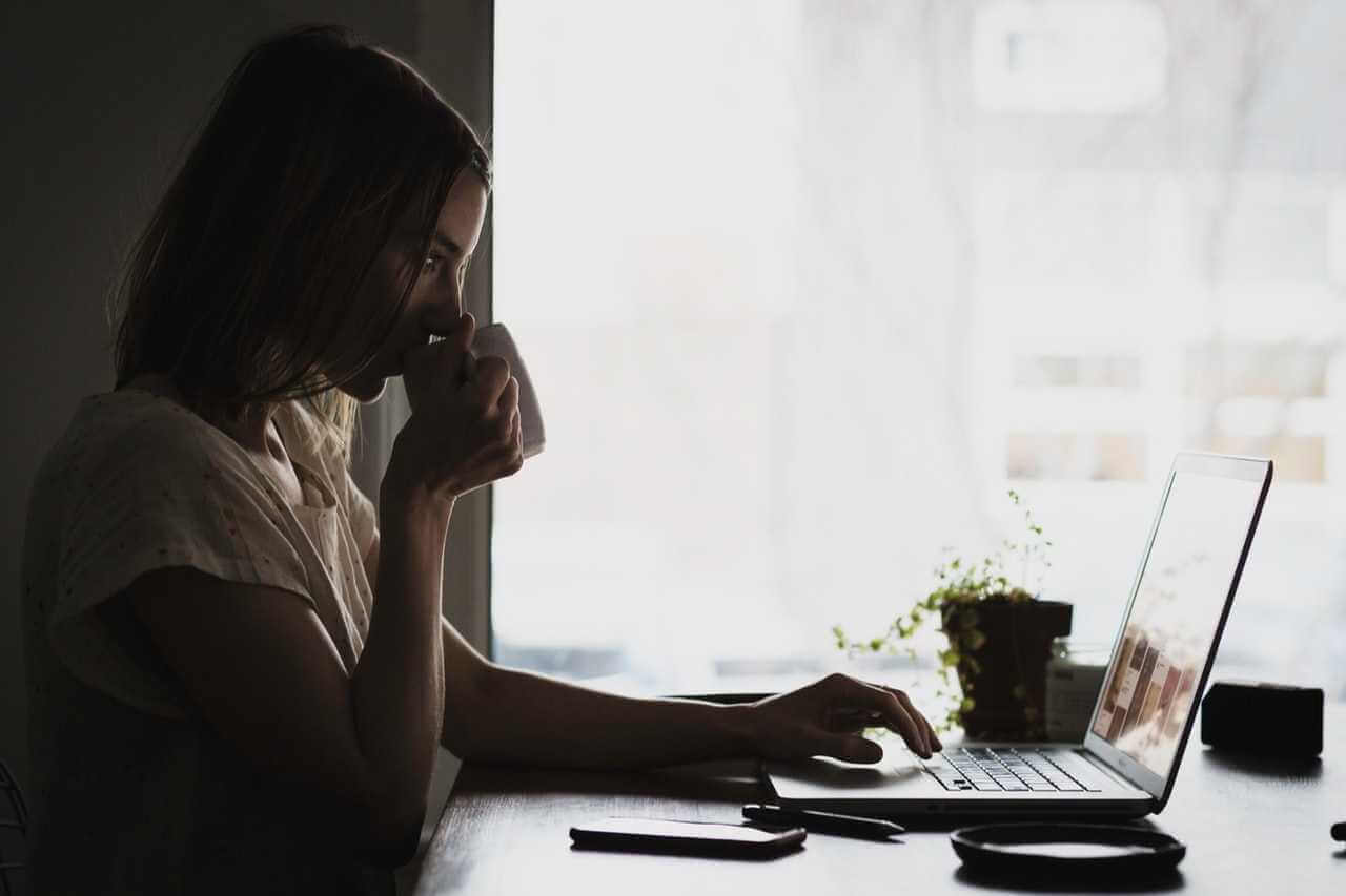 Woman working on laptop and drinking coffee.