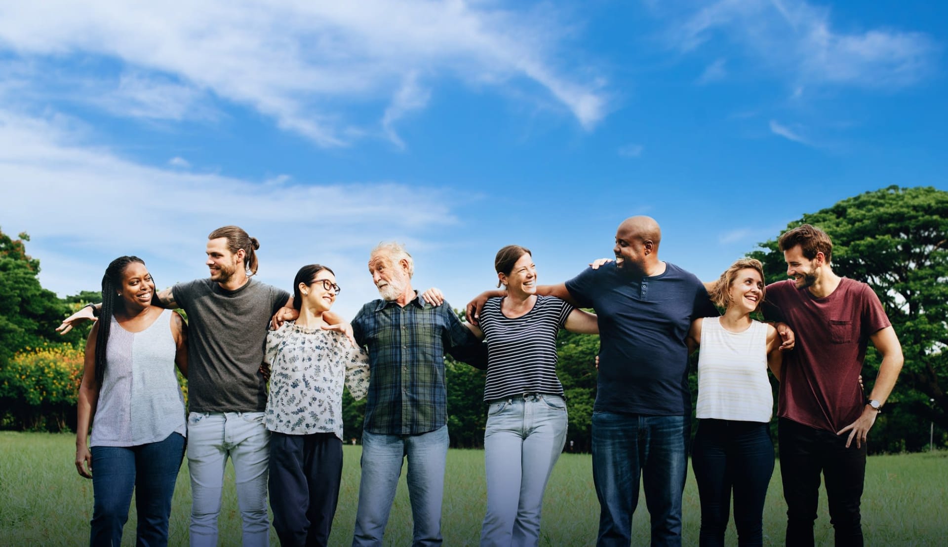 Group of smiling people standing together with their arms around each other in a park