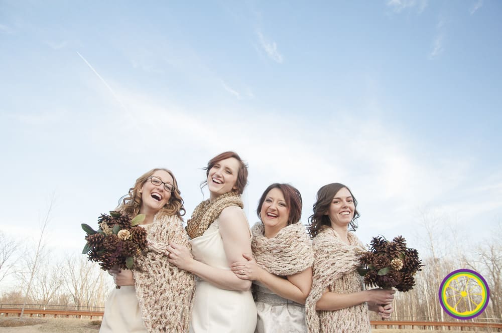 Bride laughing with bridesmaids outdoors, holding pinecone bouquets