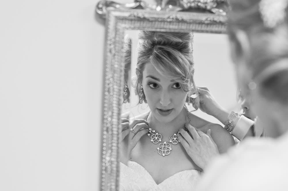 Black and white photography of a bride looking into mirror while necklace is clasped