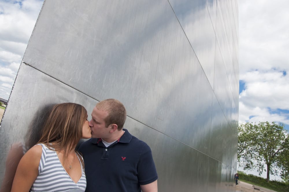 Couple posed by Gateway Arch for enagement pictures with reflection of sky