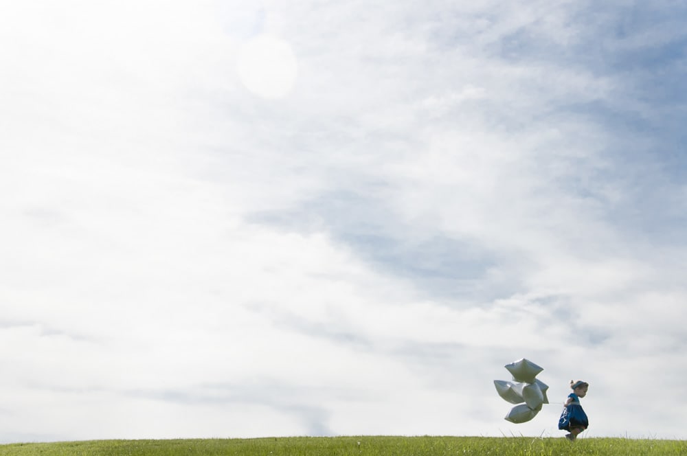 toddler girl with balloons and clouds in sky celebrating her birthday