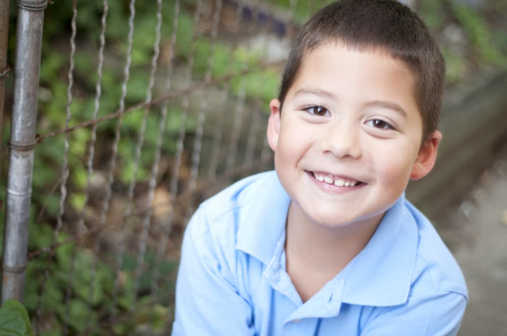 boy smiling by fence and ivy in blue shirt