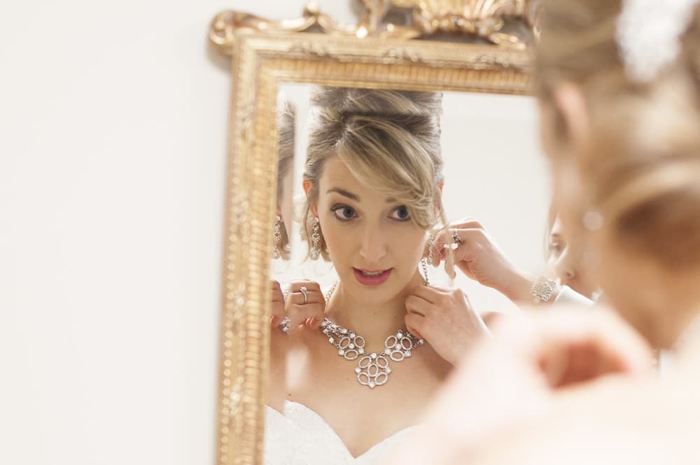 Bride adjusting necklace in golden mirror in West County MO