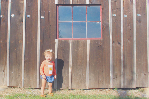 Rose in orange PSL onesie standing against barn
